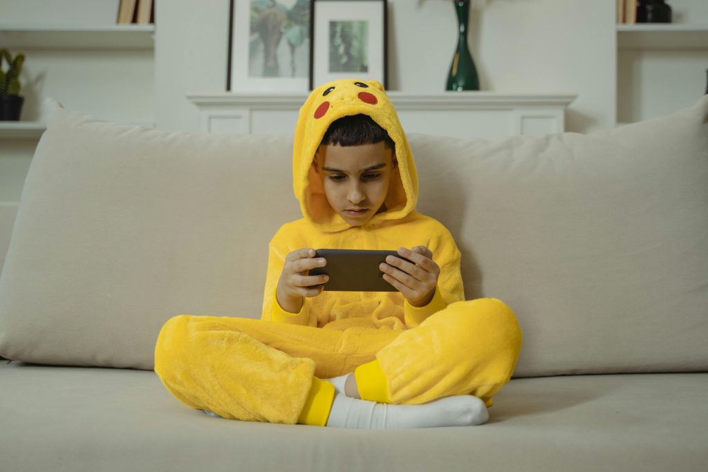 Jongen in Pikachu Onesie met smartphone (De risico’s van te veel smartphonegebruik bij kinderen)