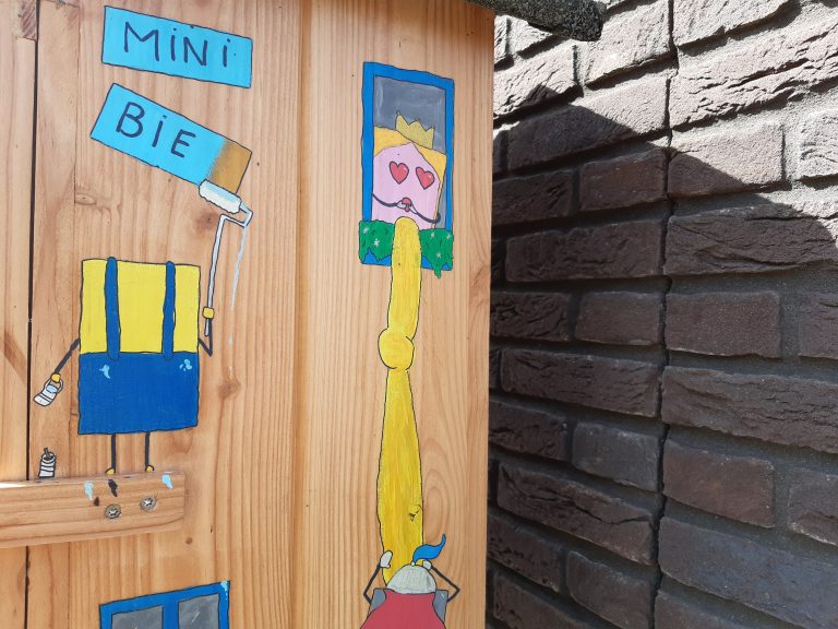 Buitenkant van de minibieb met figuren in boekvorm, zoals Rapunzel, een ridder en een schilderende minion