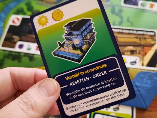 Voorbeeld van een actiekaart in the Sims Bordspel: Verblijf in Strandhuis met extra actie: Resetten. Verwijder de onderste rij kaarten in het aanbod van actiekaarten