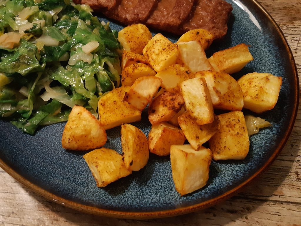 krokante aardappels als bijgerecht op een bord met vlees en andijvie