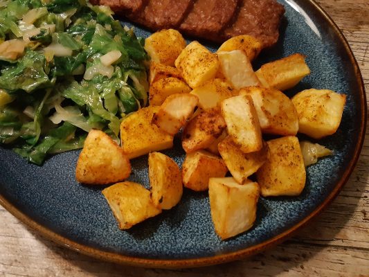 krokante aardappels als bijgerecht op een bord met vlees en andijvie
