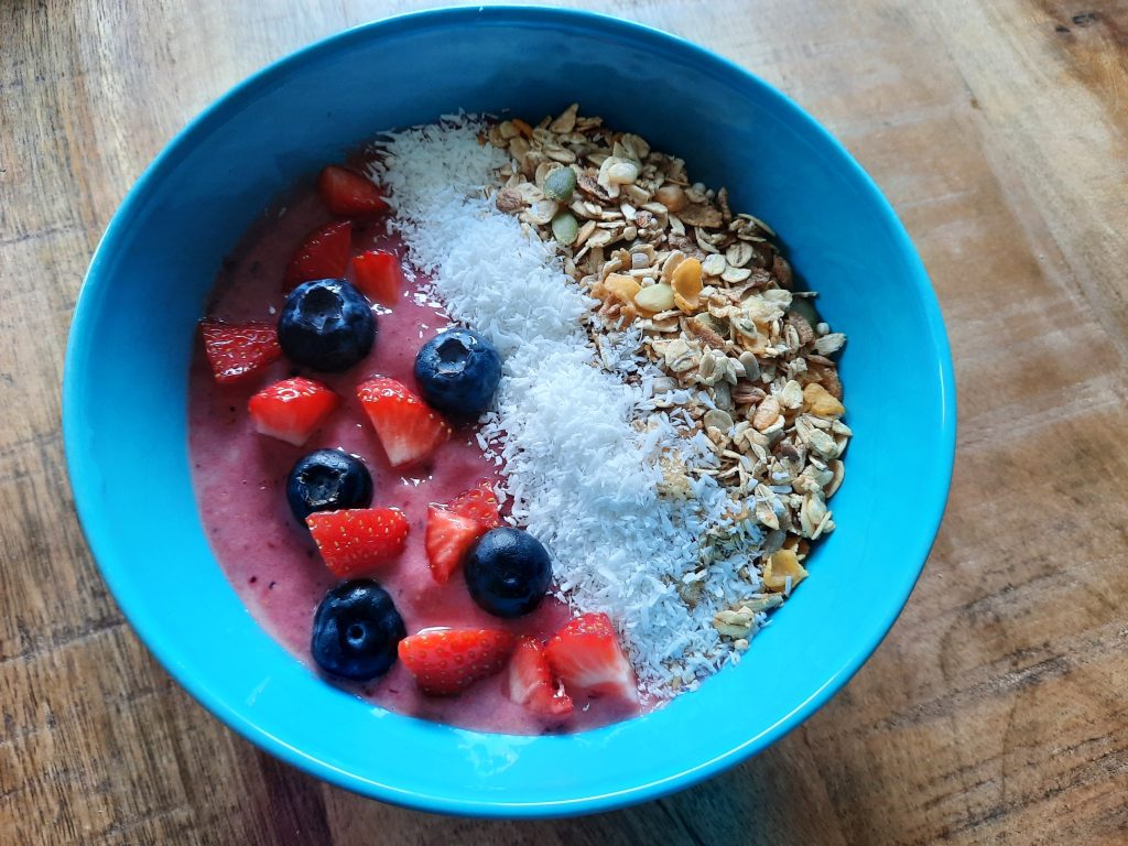 smoothiebowl met rode vruchten, granola en kokos in een blauwe kom - zomers recept