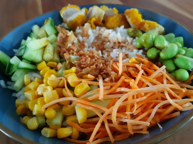 pokebowl met krokante kip, sojabonen, wortels, komkommer en sushi rijst in een kom. Wat meer ingezoomd op de wortels