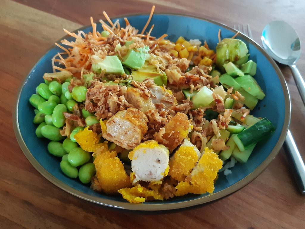 pokebowl met kipcorn, sojabonen, wortels, komkommer en sushi rijst in een kom