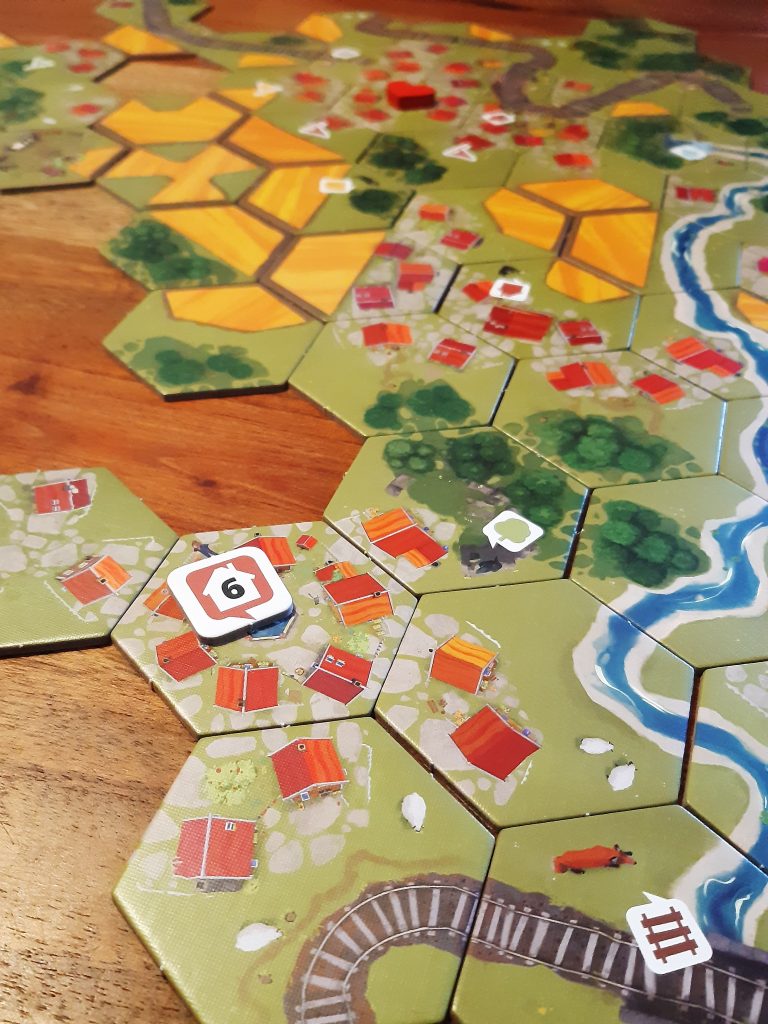 De tegels van het coöperatieve bordspel Dorfromantik op de tafel met rails, water, steden, bossen en missies met getallen erop.