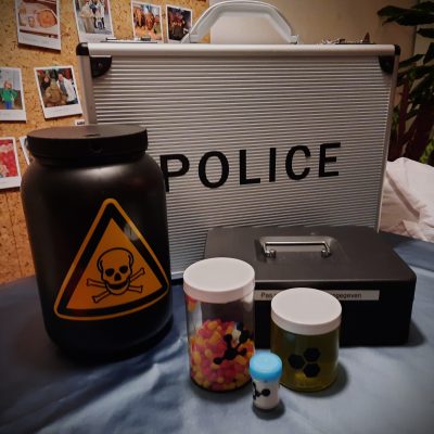 Spelmaterialen van Codekrakers: Politiekoffer, doosje met pillen, doosje met poeder, doosje met vloeistof en een grote doos met een doodskop erop